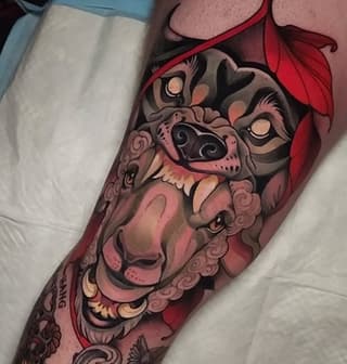 Lion and smaller feline face tattoo with ornamental scrollwork in red, pink, and black on the upper arm and shoulder.