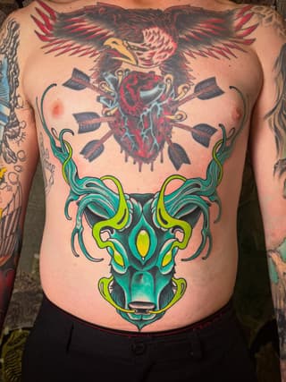 Chest tattoo featuring a winged eagle with a bleeding heart at the top and a teal bull head with lime green and yellow accents below.