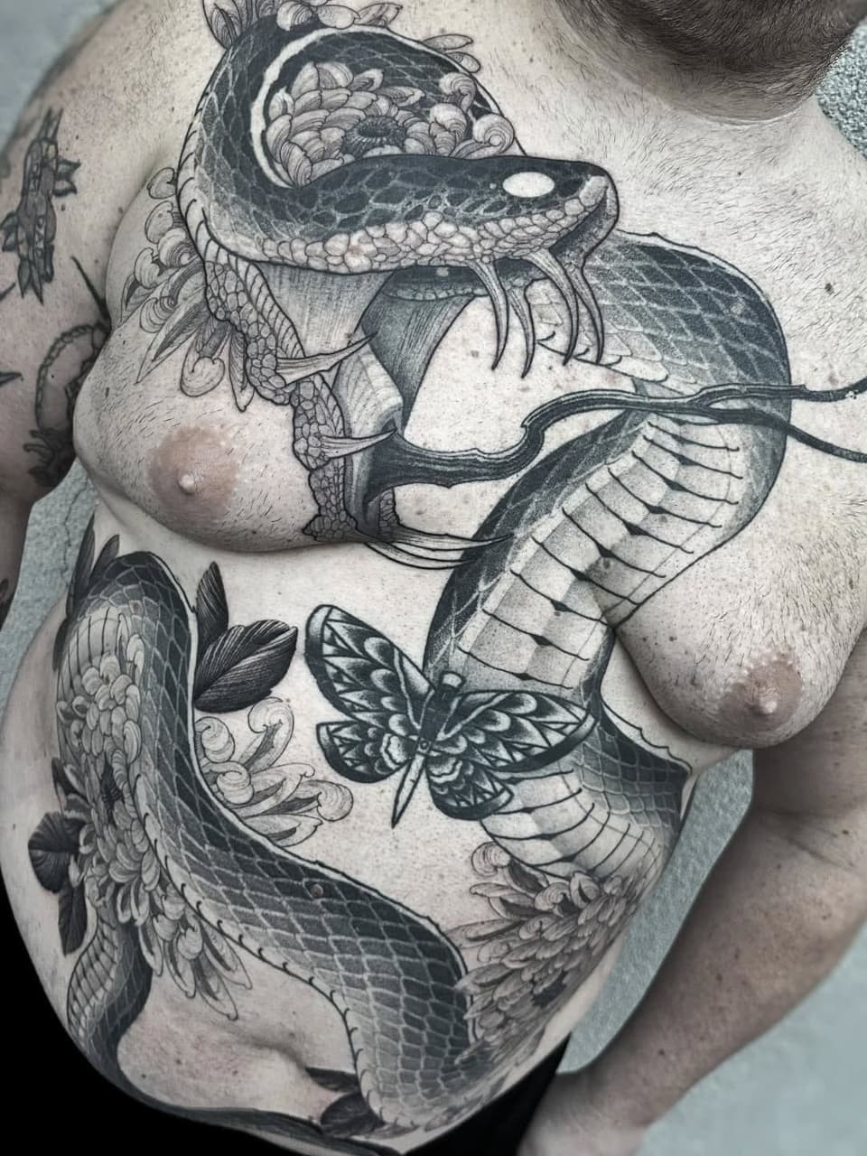 Large detailed chest tattoo featuring an orca whale with ornate floral and scroll details, accompanied by a moth and additional marine elements in black ink.