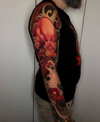Full sleeve tattoo featuring a large red lantern with ornamental scrollwork and flowering branches in red, orange, and tan tones on the upper arm.