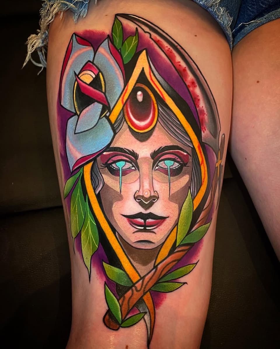 Colorful portrait tattoo on upper thigh featuring a face with third eye, teary cyan eyes, and floral elements in red, purple, yellow, orange, and green.
