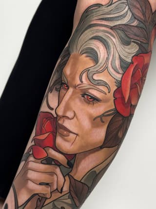 Colored shoulder tattoo featuring a woman's profile with styled hair, red flowers, and detailed facial features in browns, reds, and neutral tones.