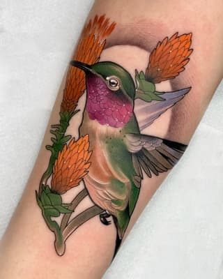 Colorful hummingbird tattoo on forearm with orange flowers, featuring green, purple, and tan plumage against skin.