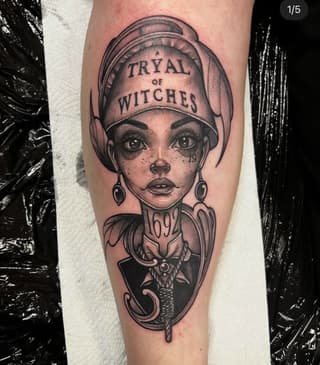 Portrait tattoo on forearm depicting a woman wearing a bonnet labeled "Trial of Witches" with ornate decorative elements below, rendered in black and grey ink.