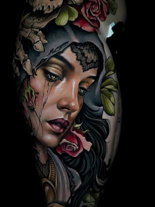 Colored tattoo on leg featuring a woman's face with tears, lace forehead detail, and surrounding flowers in red, green, and gold tones.