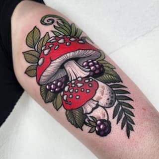 Colorful arm tattoo featuring red mushrooms with white spots, blackberries, green leaves, and a decorative swirl, arranged vertically on the upper arm.