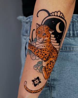 Orange spotted leopard climbing a crescent moon with decorative swirls and a small flower symbol on the inner forearm.
