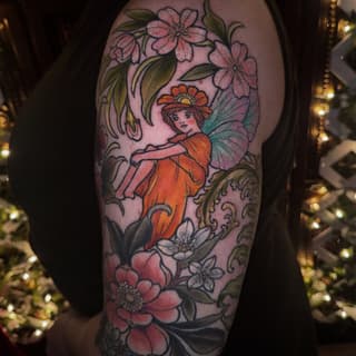 Colorful fairy tattoo on upper arm featuring a winged figure in orange dress surrounded by pink and white flowers with green foliage.
