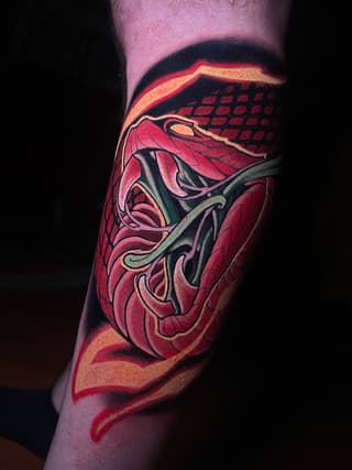 Vibrant red and gold anatomical heart tattoo on the calf with black outlines and decorative flourishes.