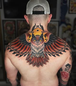 Detailed colored owl with spread wings and ornamental designs spanning the upper back and shoulders, featuring red, orange, black, and yellow tones.