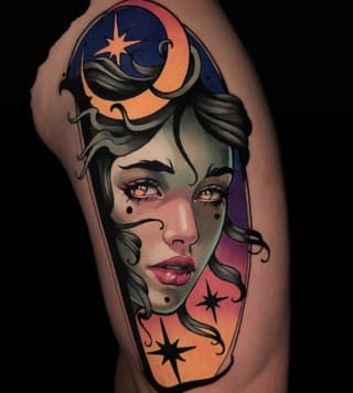 Colorful shoulder tattoo featuring a woman's face with celestial imagery including moons and stars in orange, blue, and purple tones.