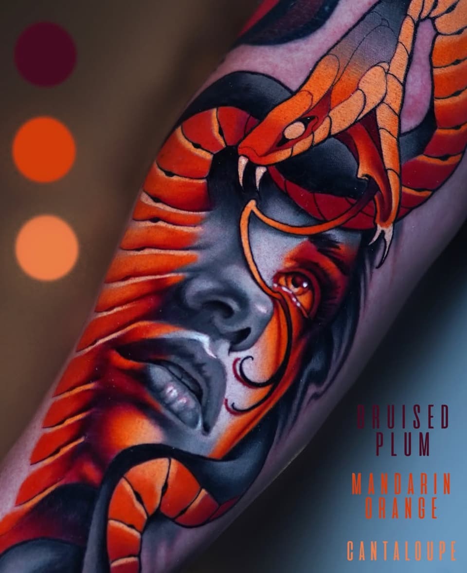 Colorful tattoo on an arm featuring a demon face with red and orange scales, black shading, and decorative horns against pink and purple skin tones.