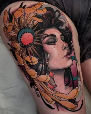 Woman's thigh tattoo featuring a female face in profile with orange flowers, a red-eyed circular ornament, black flowing hair, and teal accents.