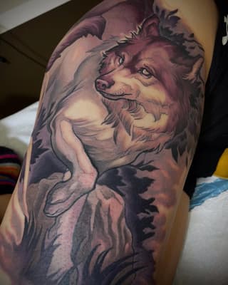 Colorful wolf head tattoo on upper arm featuring purple and pink tones with detailed facial features and fur texture.