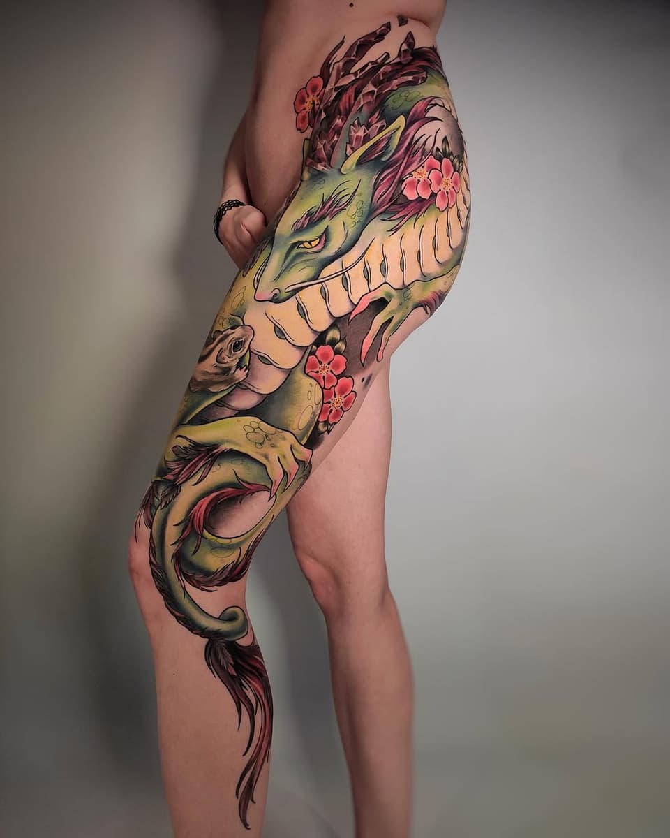 Full leg sleeve tattoo featuring a dragon with green and yellow coloring, pink flowers, and rose details, displayed on a person's thigh and calf.