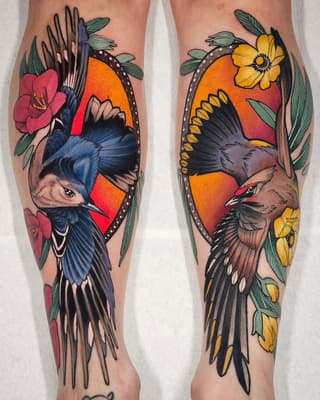 Matching pair of colorful bird tattoos on both calves featuring blue and brown birds with red and orange circular backgrounds, surrounded by pink and yellow flowers with green leaves.