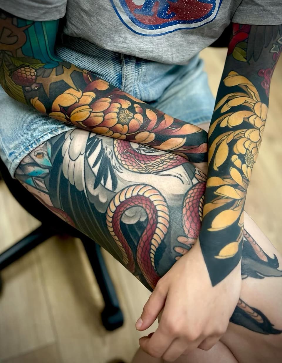 Colorful arm tattoo featuring a fish with detailed scales, a bird with extended wings, and golden floral elements on dark background.