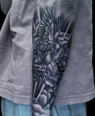 Detailed winged bird tattoo on forearm rendered in shades of gray and black ink, showing intricate feather work and dimensional shading.