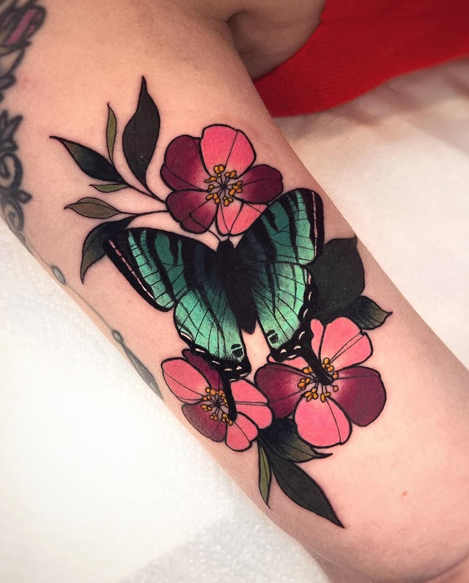 Butterfly with green and black wings surrounded by pink and burgundy flowers with green leaves on the upper arm.