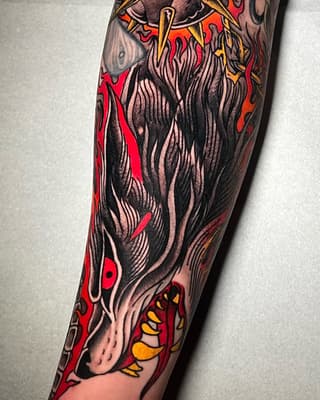 Colorful tattoo on a forearm featuring a bearded figure with flowing hair surrounded by red flames, yellow accents, and ornamental details.