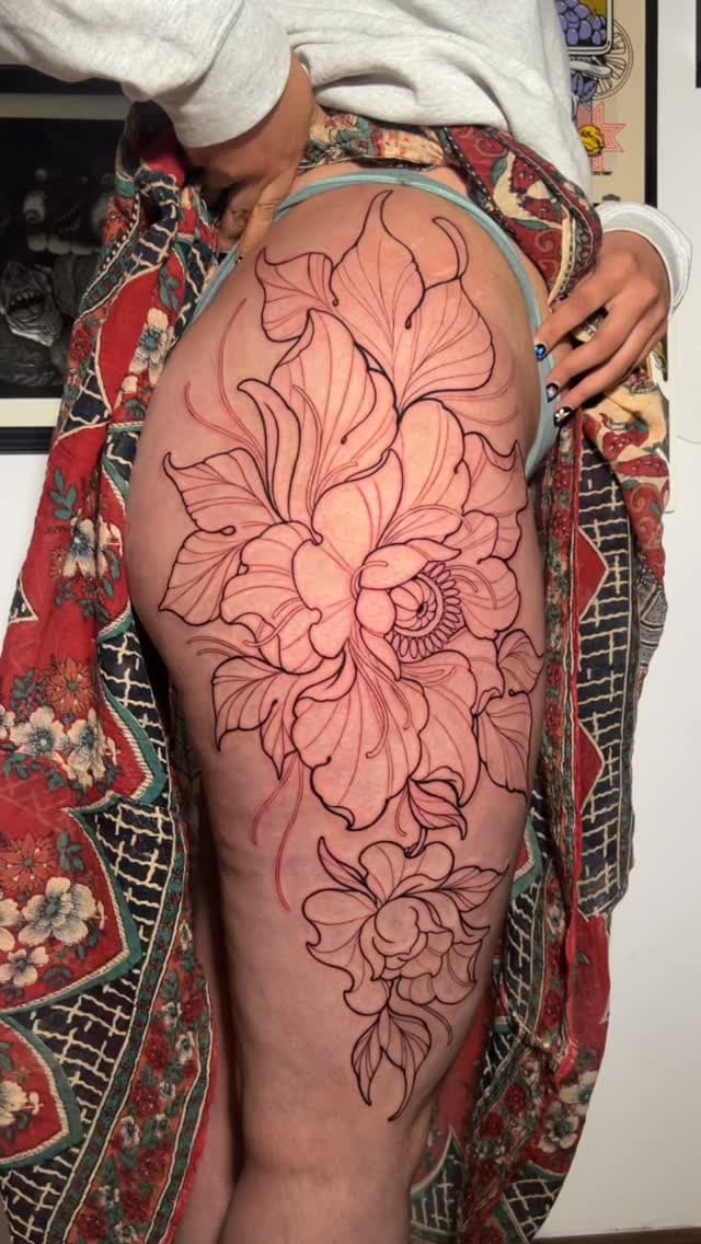 Large-scale floral leg tattoo featuring interconnected blooms in black outline on the thigh, with warm peachy-pink shading throughout.