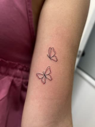 Two delicate butterflies with outlined wings in red and black ink on the forearm.