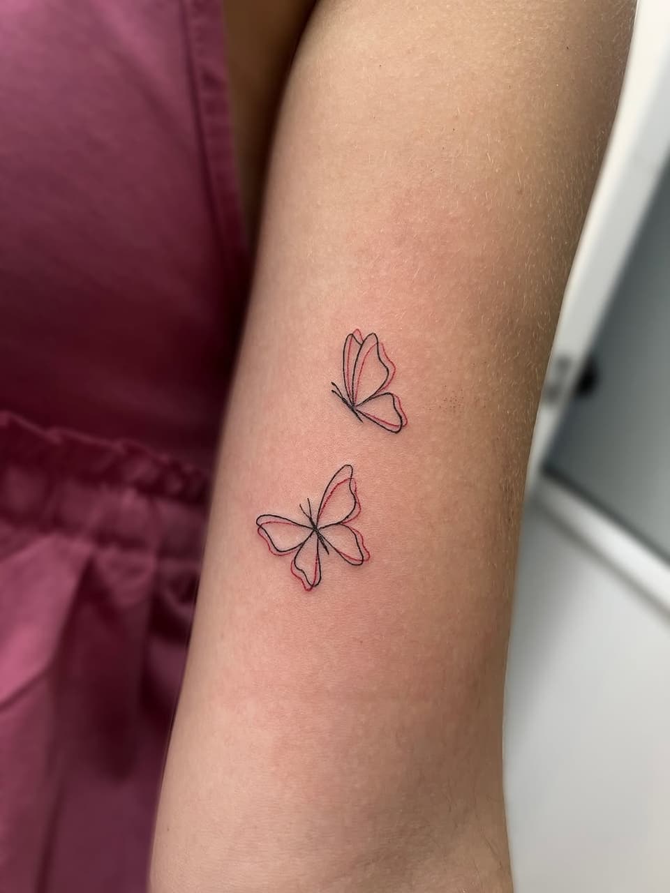 Two delicate butterflies with outlined wings in red and black ink on the forearm.