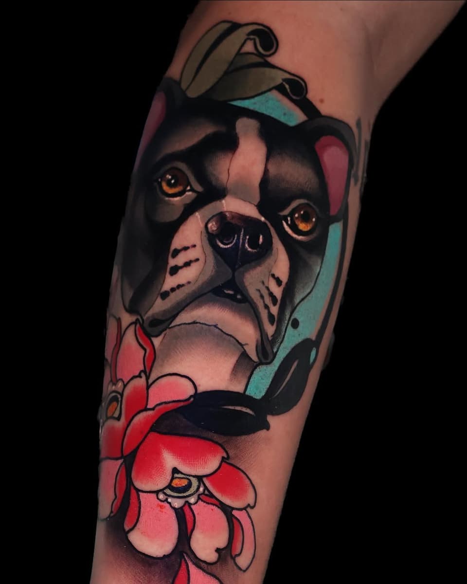 Boston Terrier head tattoo on forearm with bright red flowers below, featuring orange eyes, tan and black coloring, and teal background accents.