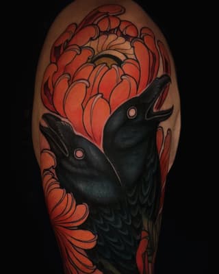 Black raven with pink eyes gazes upward surrounded by large red and orange flowers on upper arm tattoo.