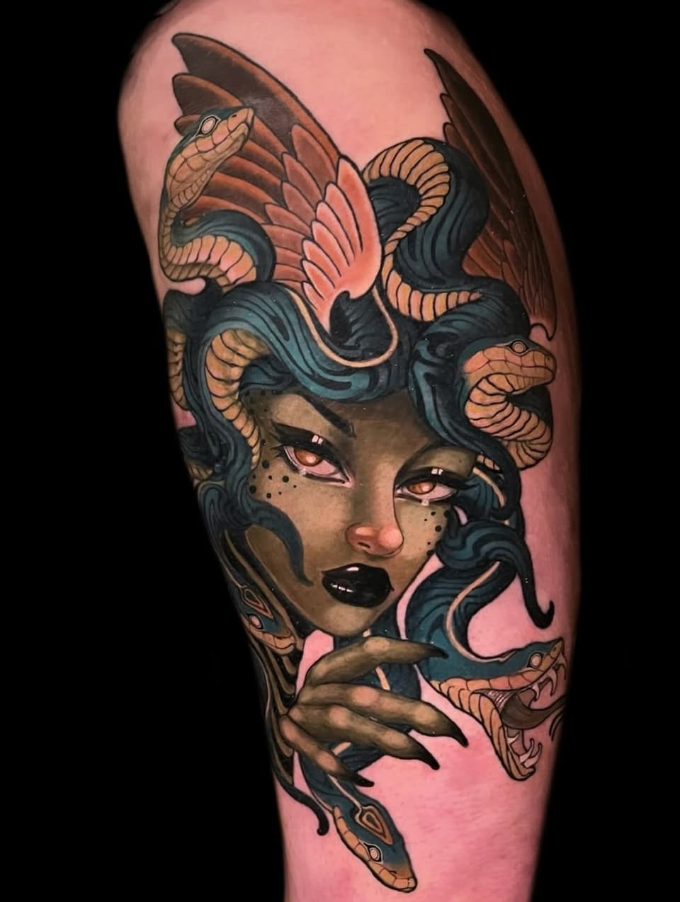 Colorful shoulder tattoo featuring a female face with dark blue hair, orange and tan snakes, and orange eyes on pink skin.