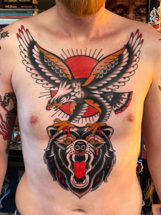 Chest tattoo featuring a red-winged eagle perched above a snarling bear head, rendered in black outlines with red and orange accents.
