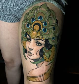 Woman's profile with closed eyes and peacock feathers forming her hair, rendered in green, gold, and blue on the upper thigh.