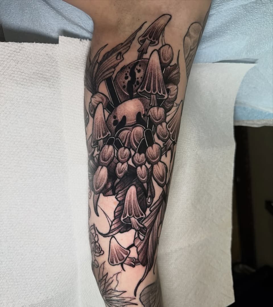 Detailed leg tattoo featuring a mushroom with spotted cap, bell-shaped flowers, and botanical elements in brown and black ink on the calf and shin.