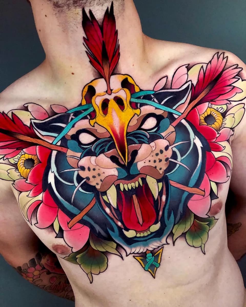 Colorful chest tattoo featuring a snarling tiger head with red feathers, yellow eyes, and pink flowers surrounding the design.
