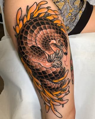 Dragon head with scaled body and orange flame-like foliage adorning the thigh and leg area in orange, black, and tan colors.