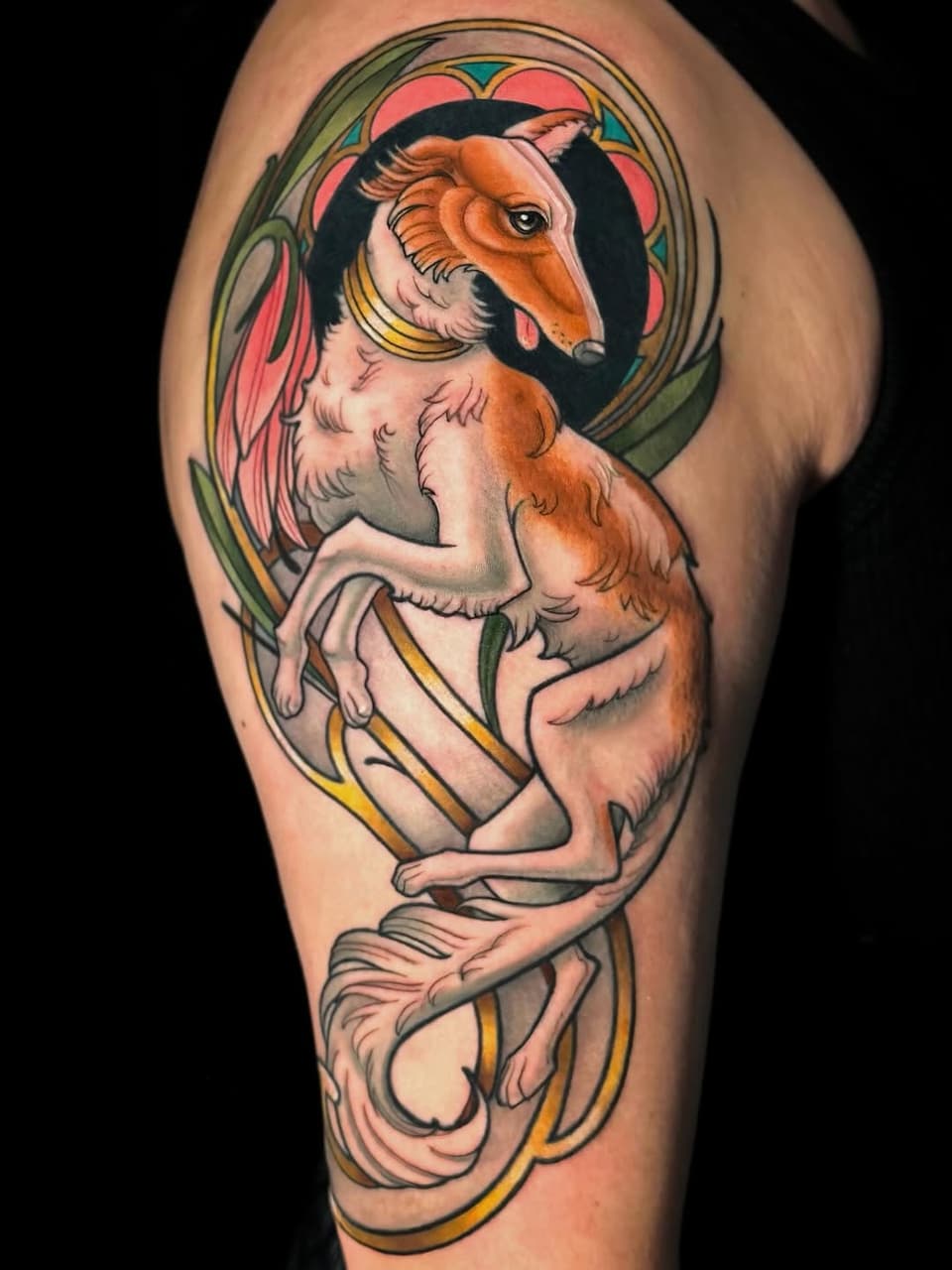 Colorful shoulder tattoo of a winged goat-like creature in a decorative circular frame, featuring orange, pink, green, and gold accents.