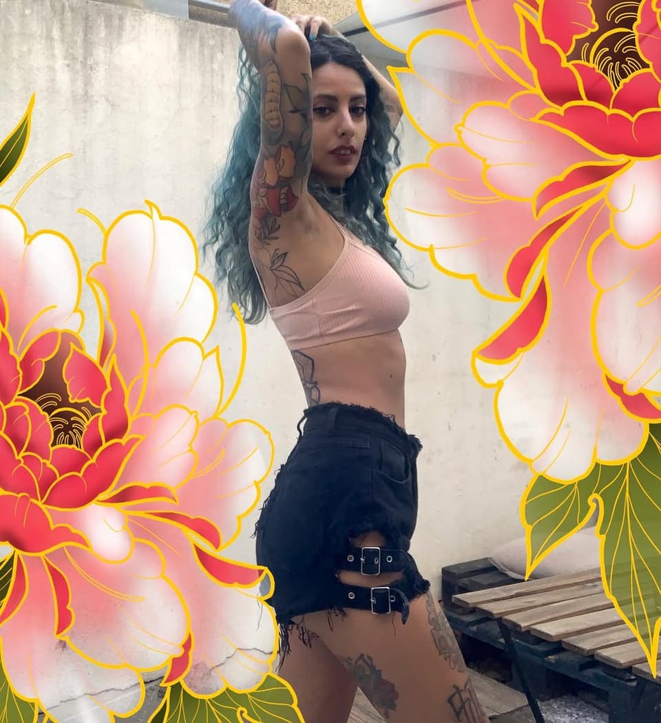 Woman displaying colorful floral and decorative tattoos on her arms, torso, and legs in shades of red, yellow, and black.