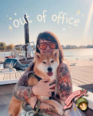 Woman with full-color floral and animal tattoos on both arms poses on a boat deck holding a smiling Shiba Inu dog.