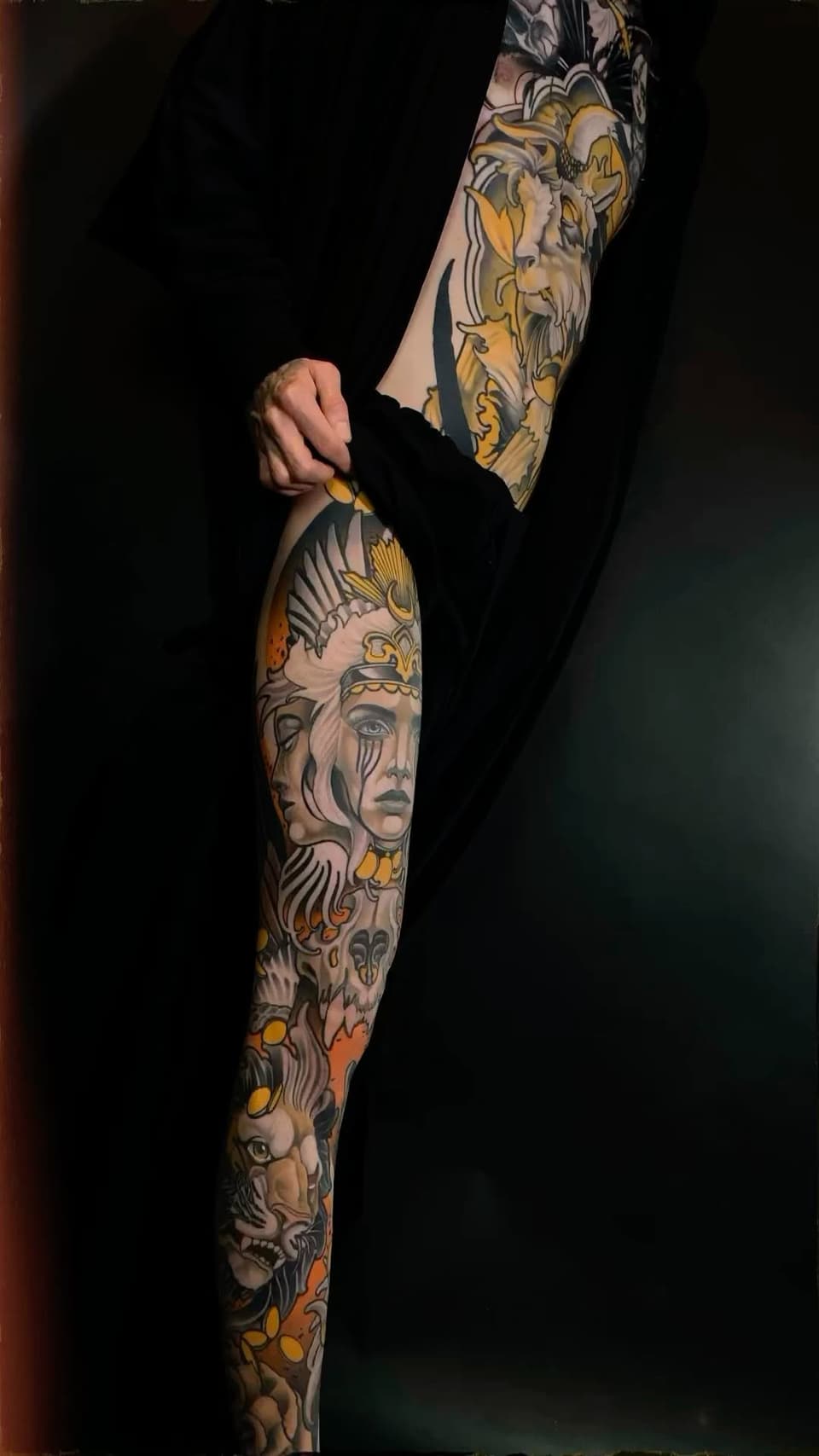 Full-length arm tattoo sleeve featuring classical portrait heads, ornamental details, and gold accents on a person's arm against a black background.