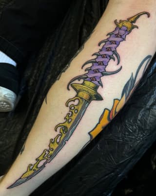 Ornate fantasy dagger tattoo with purple segmented blade, gold decorative handle, and yellow flame accents on the forearm.
