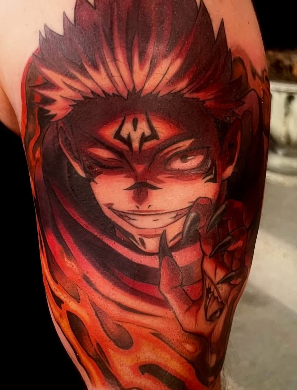 Vibrant red and orange tattoo of a grinning character with spiky hair and facial markings on the upper arm.