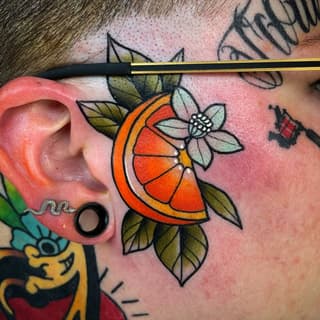 Colorful tattoo on the side of a neck featuring an orange citrus fruit slice with a white flower and olive-green leaves against pink skin.