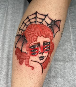 Red-haired female face with bat wings and spider web tattoo on calf, featuring red ink with black outlines and details.