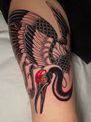 Detailed bird wing tattoo on upper arm featuring red and orange accents with scaled patterns and sharp talons in black and flesh tones.