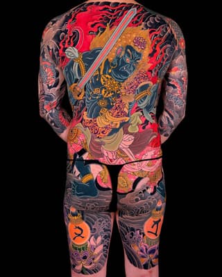 Full back and leg tattoo featuring a warrior figure with sword, ornate clothing, red clouds, dragons, and decorative elements in red, gold, blue, and black colors.