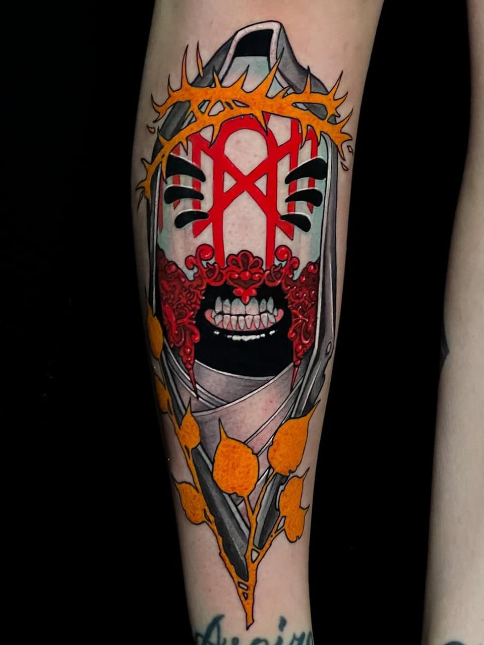 Colorful leg tattoo featuring a screaming face with a red cross, thorned crown, and orange flame-like elements surrounding a pale gray rectangular frame.