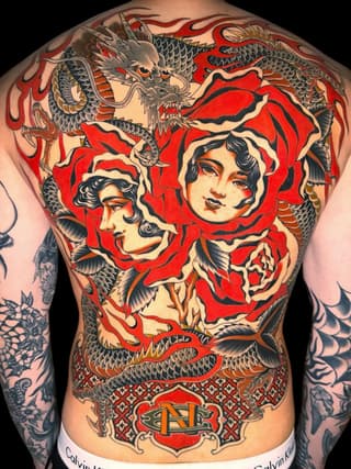 Back tattoo featuring two female faces with red head coverings, dragons, and ornamental designs in red, black, and gold ink.