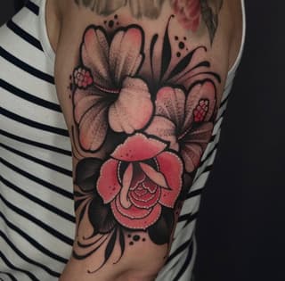 Colorful floral tattoo on upper arm featuring pink and red blooming flowers with black outlines and dotwork details on skin.