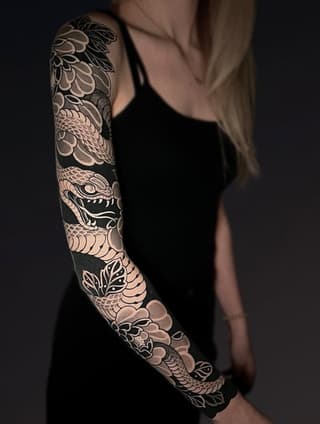 Full-sleeve arm tattoo featuring an ornate dragon with scaled body, floral patterns, and a demon mask in grayscale and tan tones.