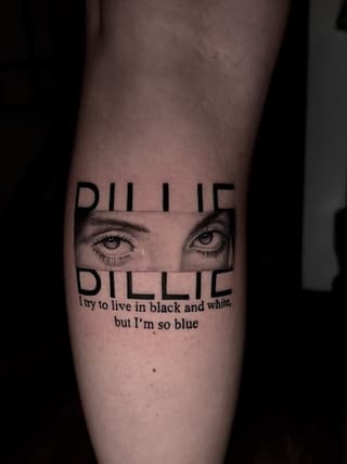 Billie Eilish tribute tattoo on forearm featuring her eyes and text "I try to live in black and white but I'm so blue" in black ink.